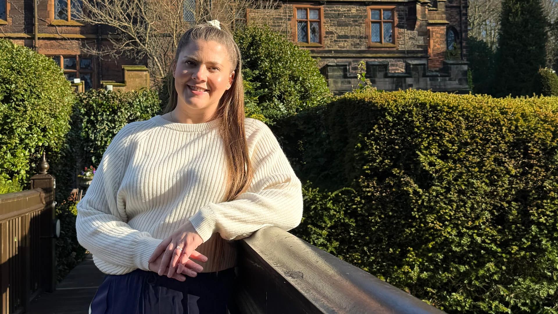 Jemma from Love Jemma, standing relaxed leaning on a bridge with a smile on her face. Ready to be your friendly face a the end of the aisle.